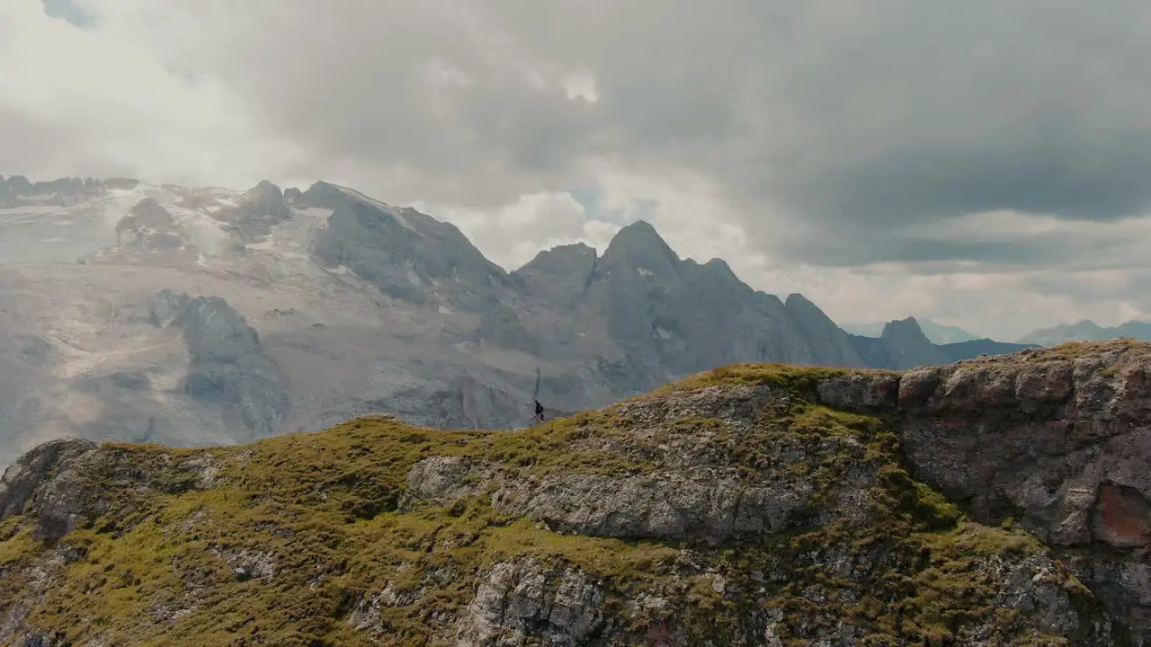 Parallax aerial shot of a explorer walking on top of a mountain ridge revealing a glacier on the top of the steep mountains in the background cinematic grade