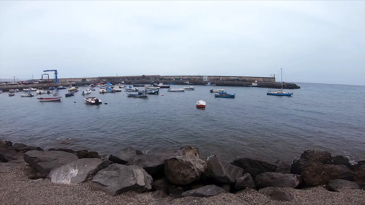 Pan to the Right with Ships Docked in a Harbor with Black Rocks