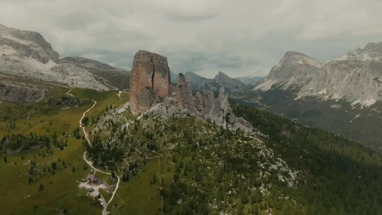 Aerial view aproaching massive rock formations with distant tall mountains in the background green fields at the bottom cloudy day cinematic color grade