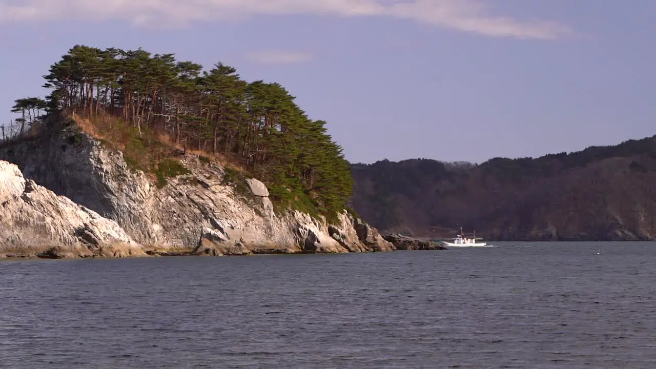 Fishing ship disappearing behind tall cliffs in distance in ocean