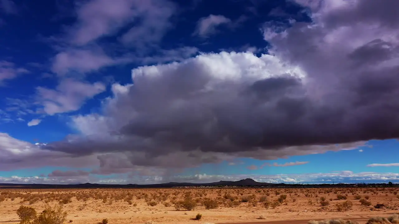 Mojave Desert with stormy rain clouds overhead and the distant mountains in silhouette sliding aerial view