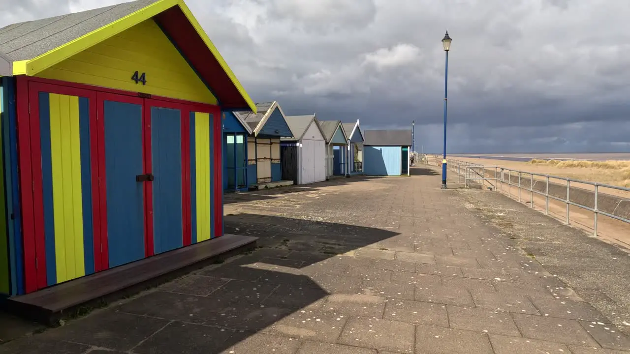 Colorful beach huts stood in a line along the seafront with sandy beach and moody grey sky’s