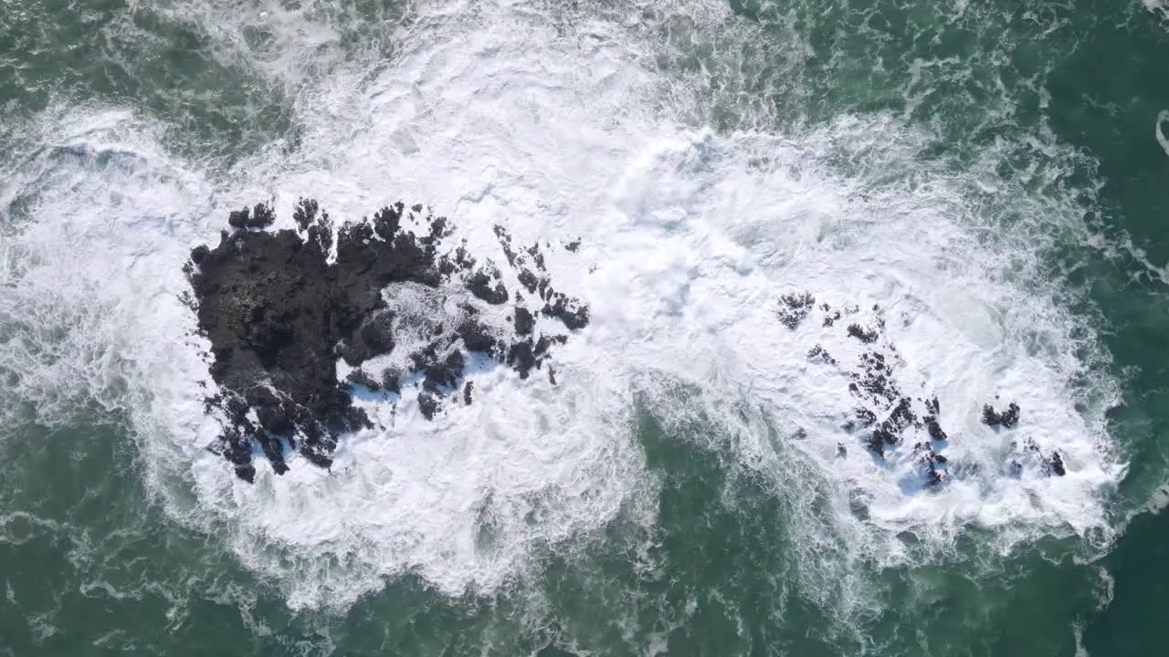 White foamy waves crash onto a coral rock in the ocean in Indonesia