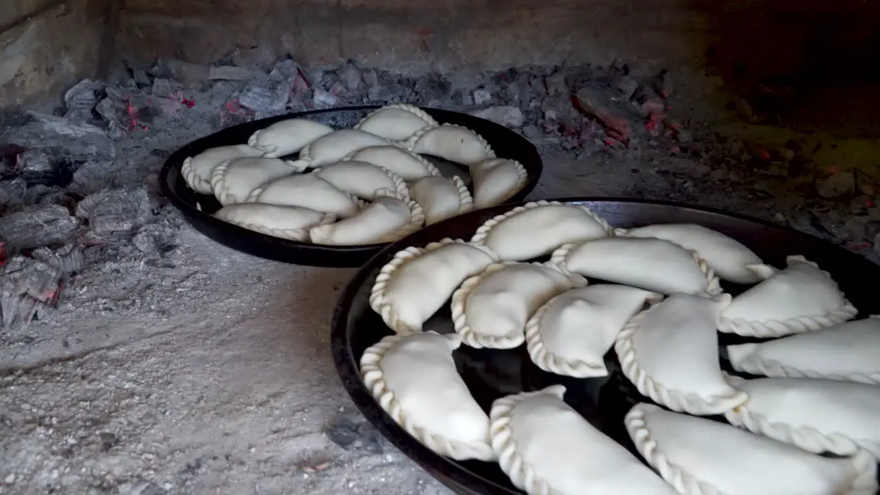 Close up shot of two trays of uncooked empanadas waiting to be cooked inside a clay oven