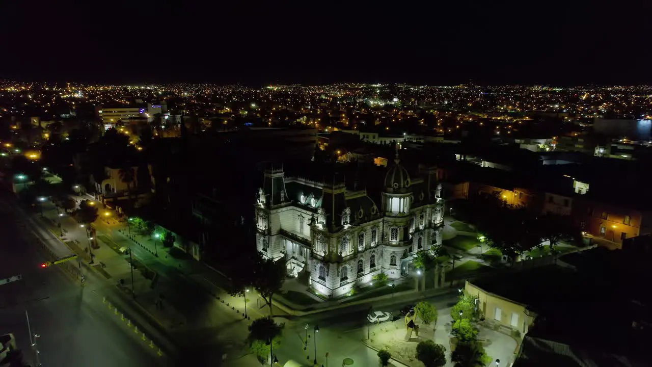 Aerial view away from the Illuminated Quinta Gameros building in Chihuahua night in Mexico reverse drone shot