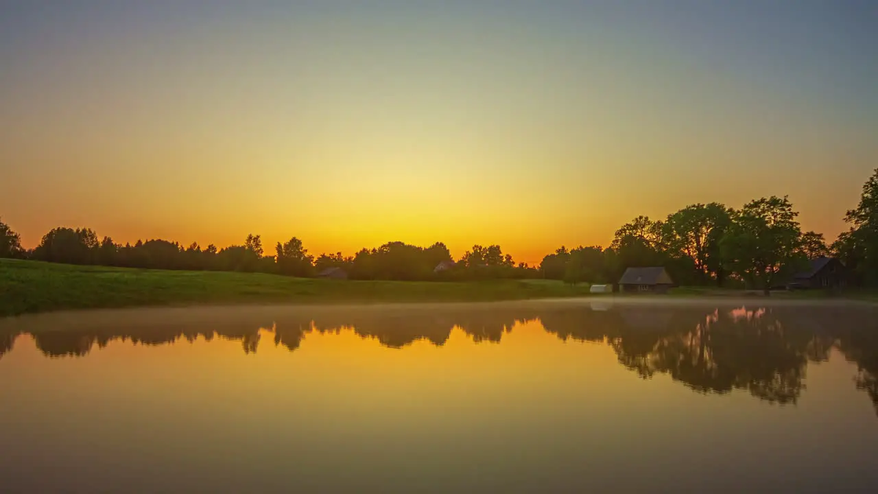 The setting sun reflecting off the still misty surface of a countryside lake sunset to nighttime time lapse