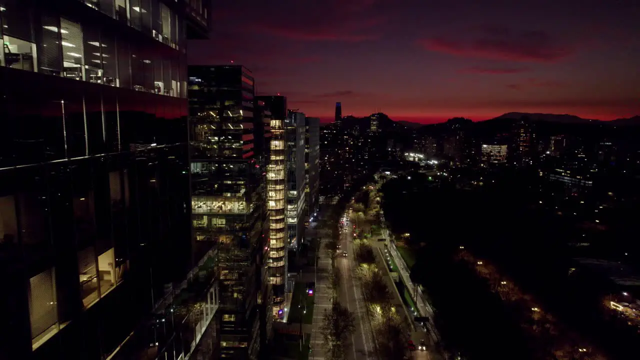 Flyover the modern buildings of Nueva Las Condes in Santiago Chile the business center of the city with the Costanera tower in the background at night with an orange sunset