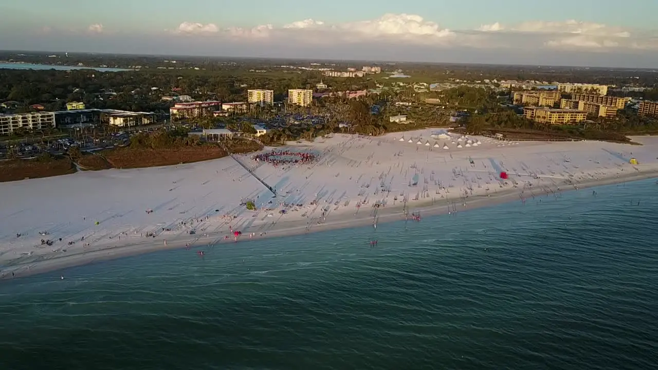 Aerial shot slow approach to scenic white sandy beaches over turquoise water on siesta key beach Florida with drum circle