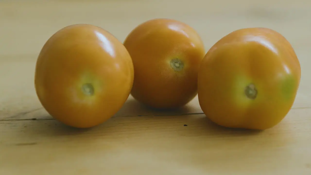 two tomatoes on wooden table another one comes rolling in