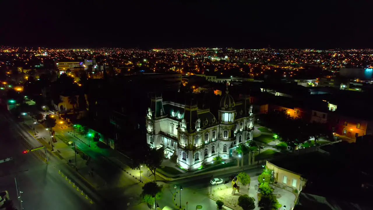 Aerial view away from the Illuminated Quinta Gameros building in Chihuahua night in Mexico pull back drone shot