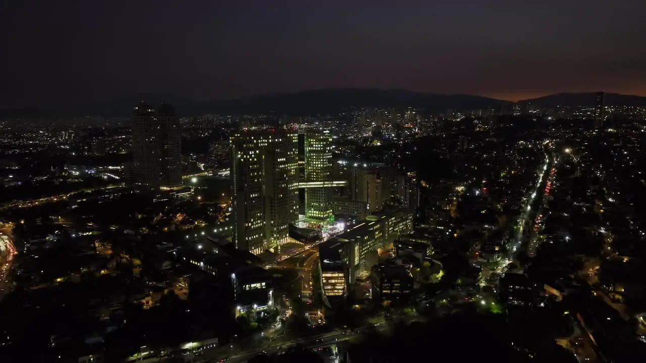 Aerial view approaching the night lit Arcos Bosques complex in Mexico city