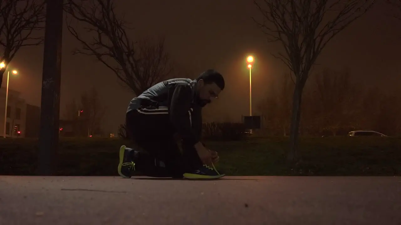 Runner ties his shoelaces in a spots track at night time