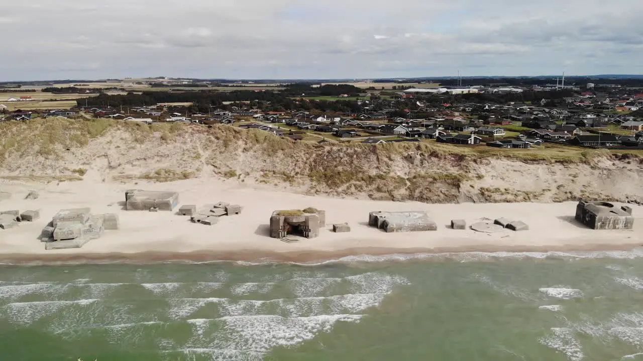 Aerial of beautiful white sand beach with old abandoned German bunkers in the sand wile waves crashes and houses in the distance