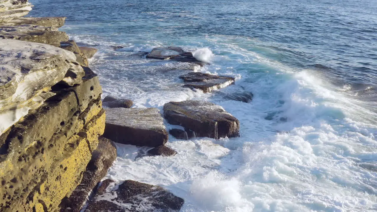 Large waves crashing onto ocean rocks POV drone moving forward along cliff face Coogee Beach Sydney Australia