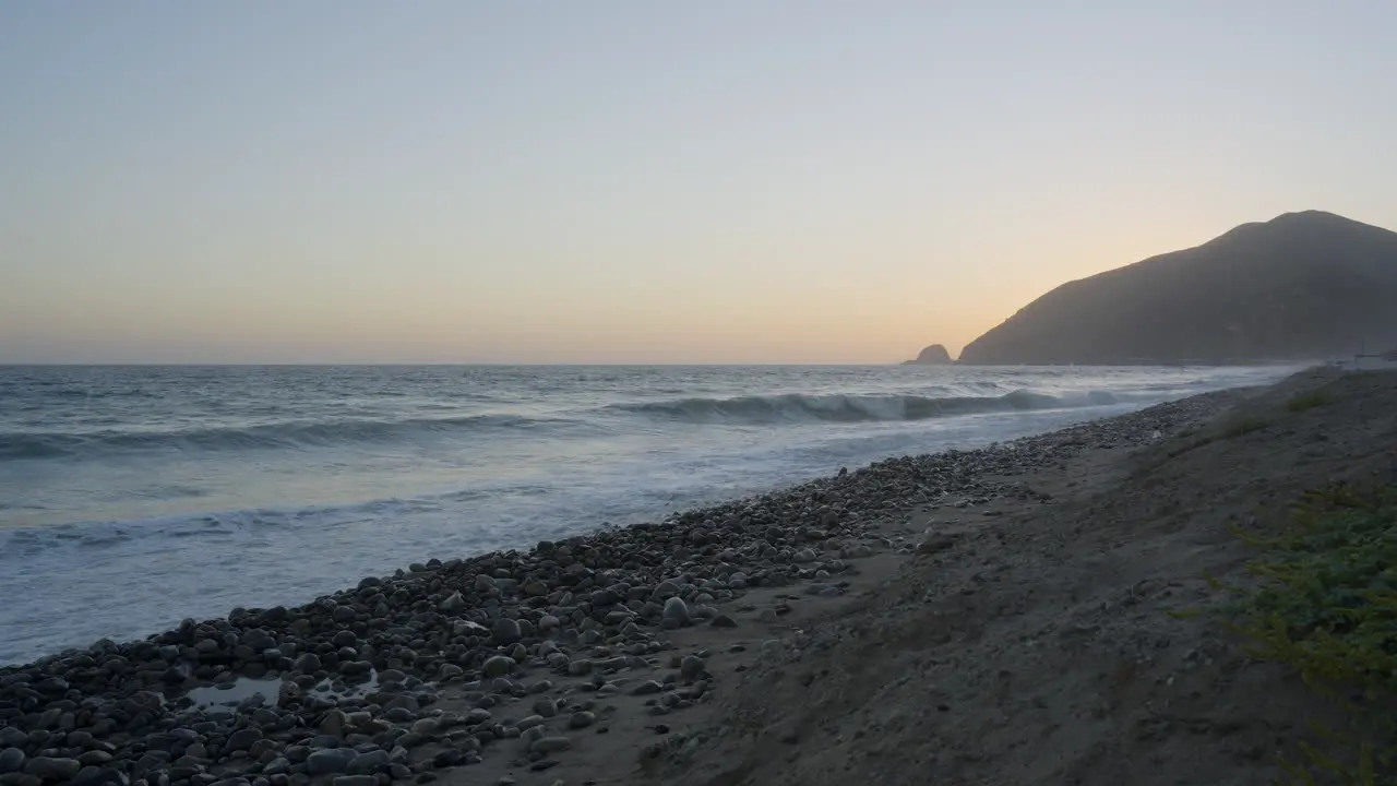 Stationary shot of waves rolling through the Pacific Ocean with the sun setting behind a distant mountain located in Southern California