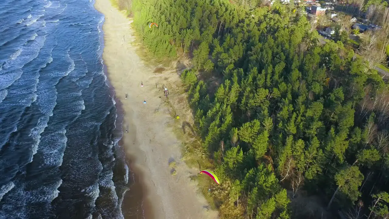 Aerial view of parasailers and tourists on beach with calm waves reaching the shore sunny day