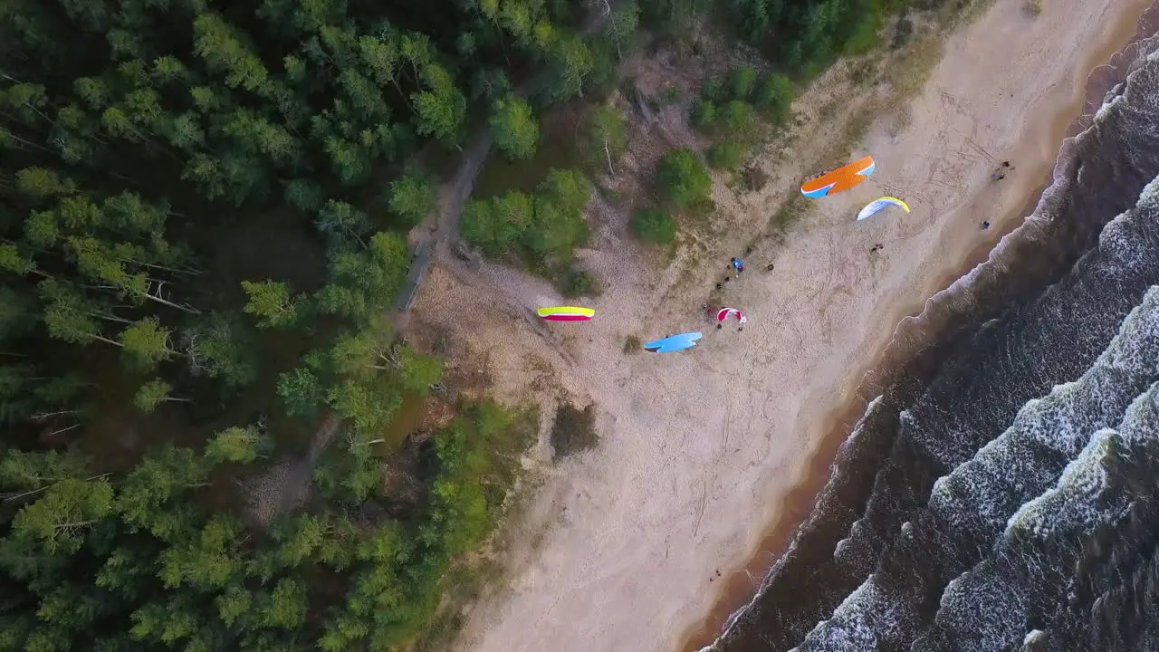 Aerial top down view of tourists enjoying parasailing on sandy beach with calm waves reaching the shore