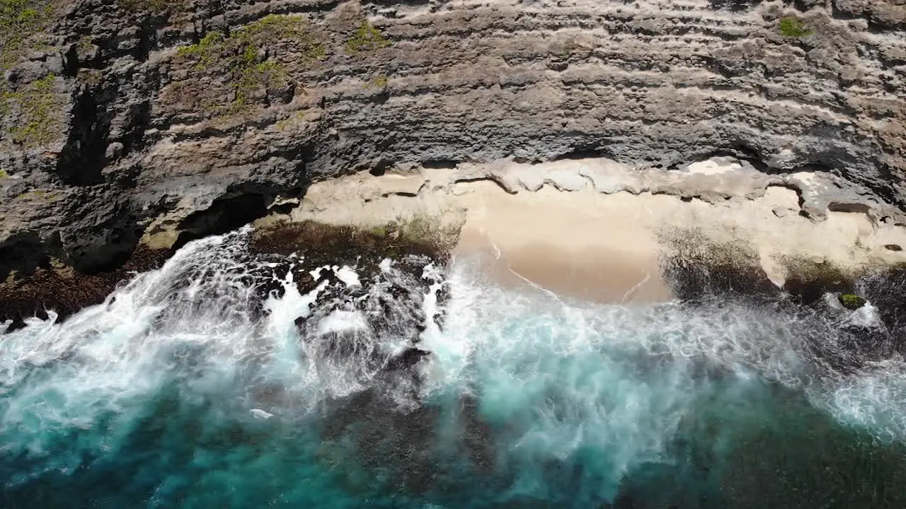 Aerial view of waves rolling onto the beach below a cliff in Uluwatu Bali