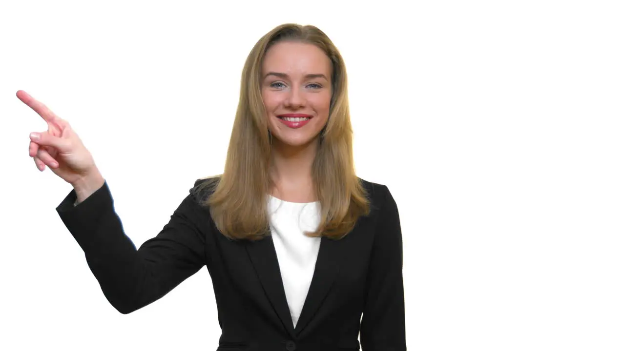 A close-up of a woman smiling and pointing off to the side then lowering her arm back down to her side on a seamless white studio background