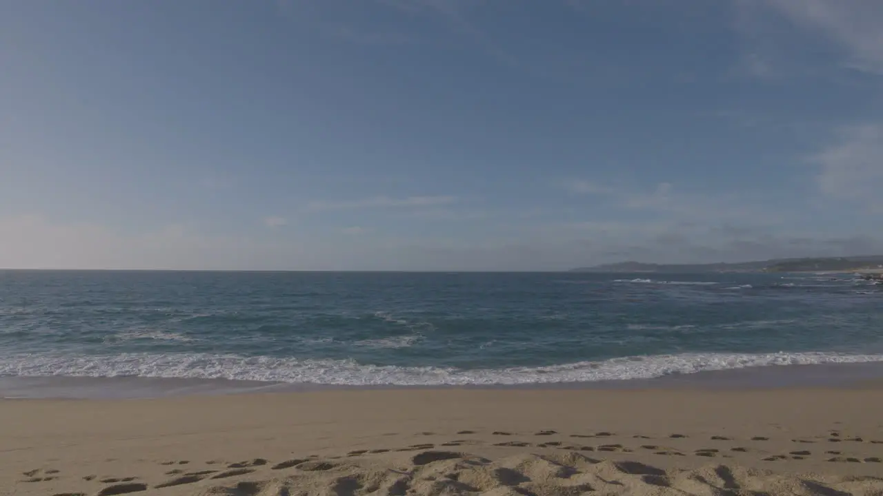 Slow motion panning shot of the beach and waves on a sunny day at California Monterey Bay Marina State Beach