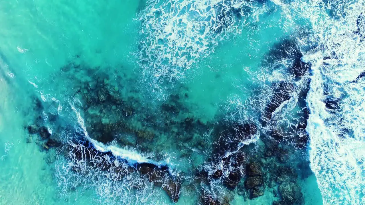 4k aerial drone shot of beautiful tropical blue ocean with waves breaking on rocks