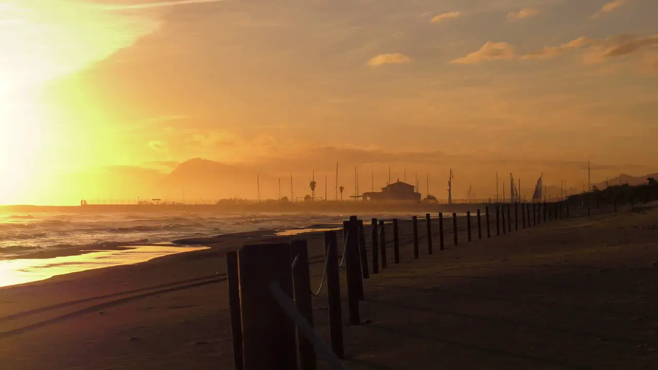 Deserted sandy beach and dunes at sunrise with waves breaking on shore harbor in background