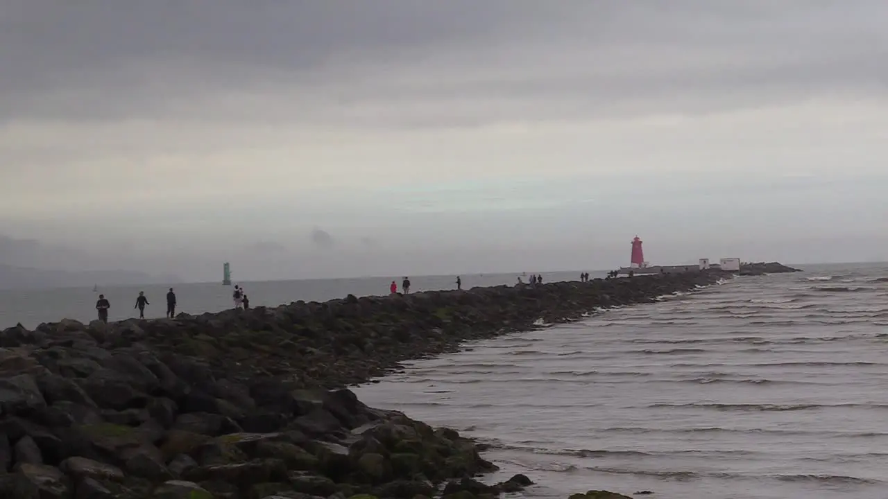 People walking along the coast or south wall to a lighthouse on Dublin's coastline