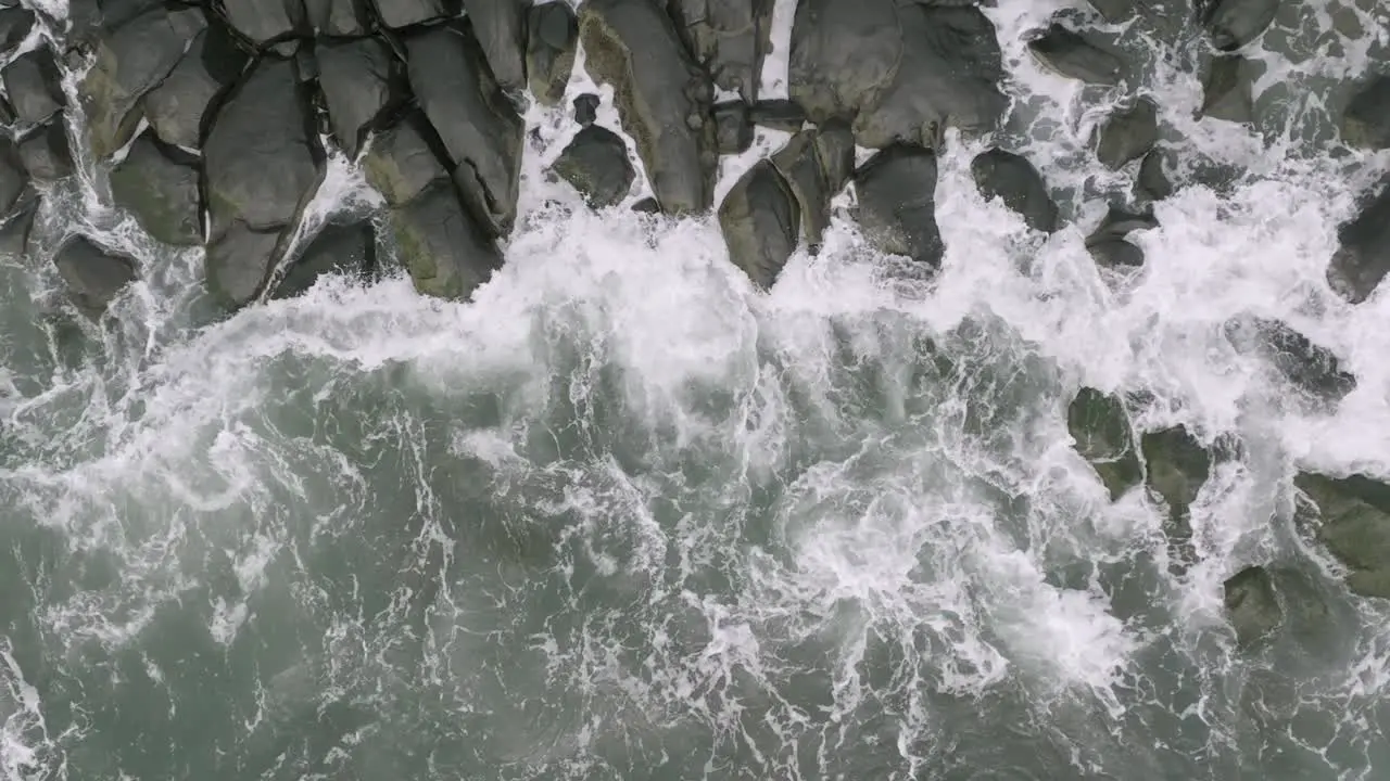 Slow motion aerial overhead top down footage of ocean waves crashing into rocks that are on the coast