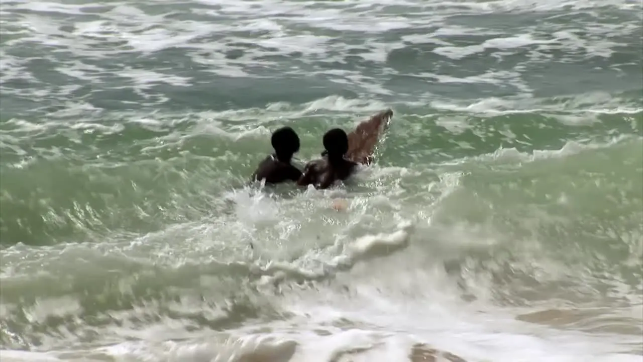 Two nigerian kids surfing witha makeshift board