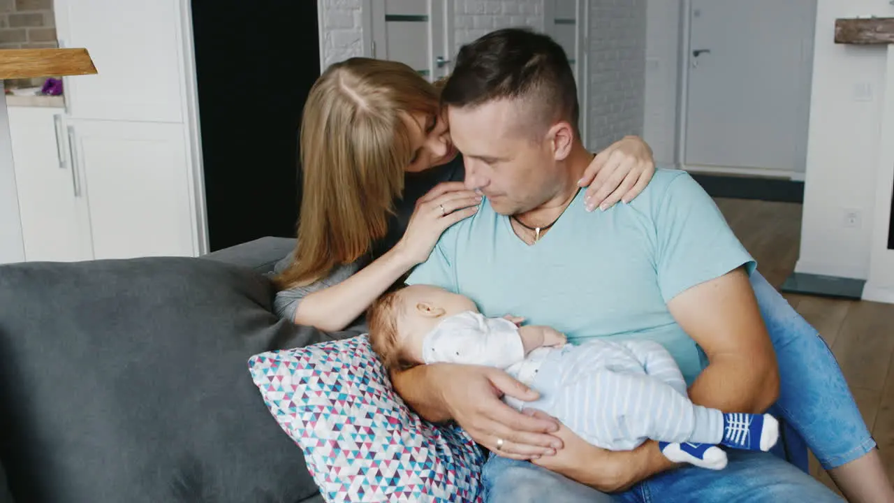 Young Woman Affectionately Hugging Her Husband Who Is Holding In Their Hands Two-Month Son