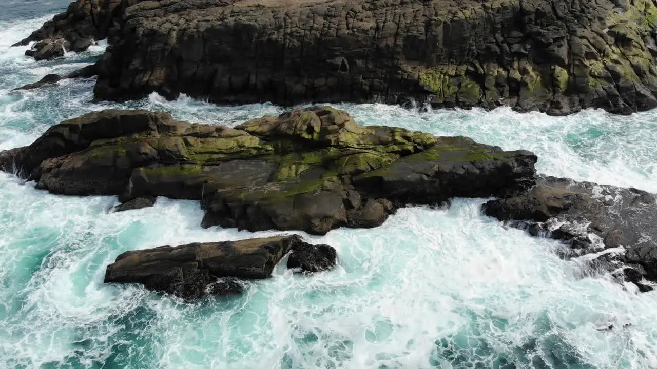 Drone looks down over sea rocks as waves crash into it