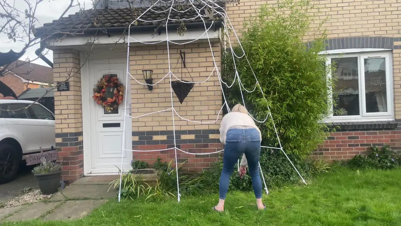 Woman prepares her garden for Halloween with large replica Spider web