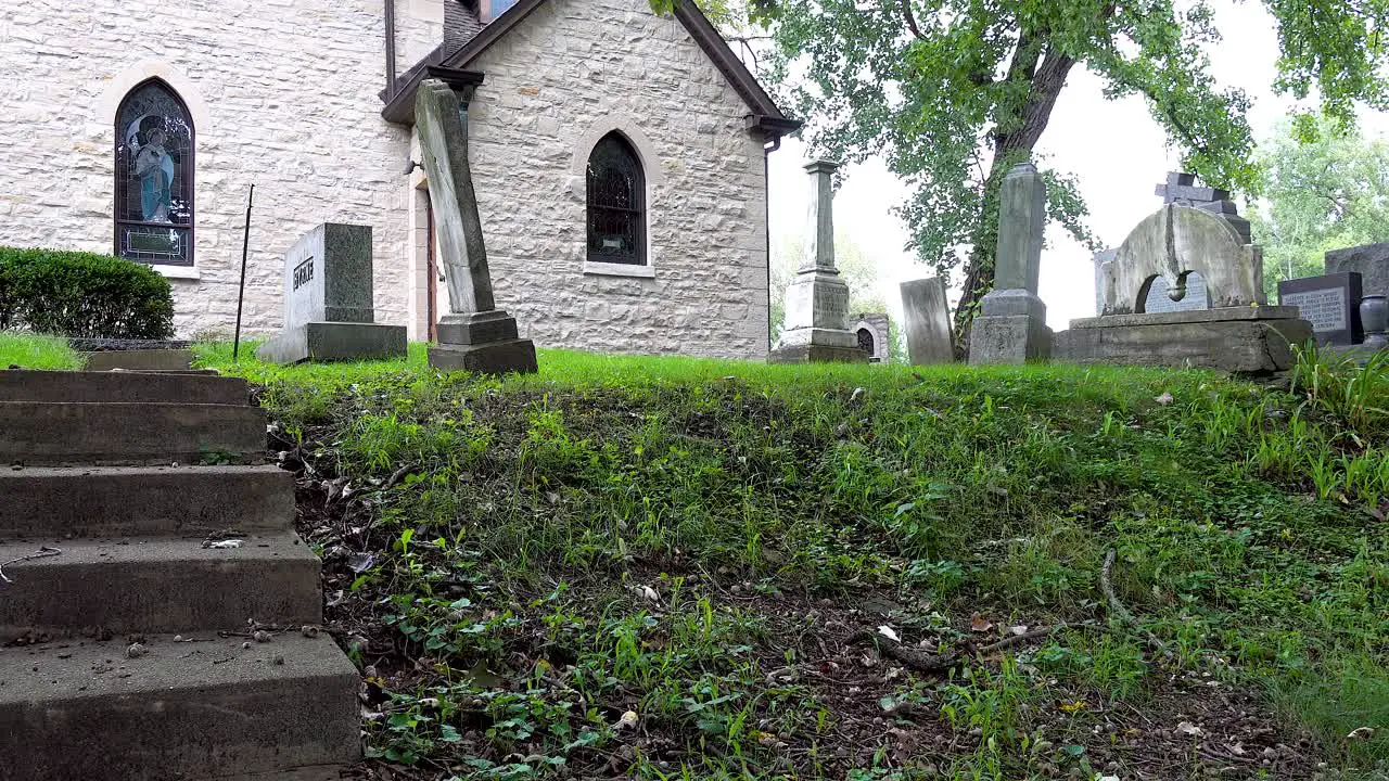 panning shot of gravestones with a hilltop church in a very old cemetery with many trees 4k