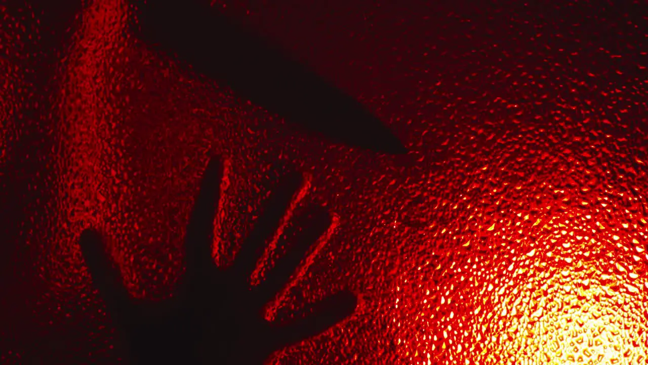 Terrifying silhouette of possessed killer creeps on glass slowly opens door in the dark under ominous red light