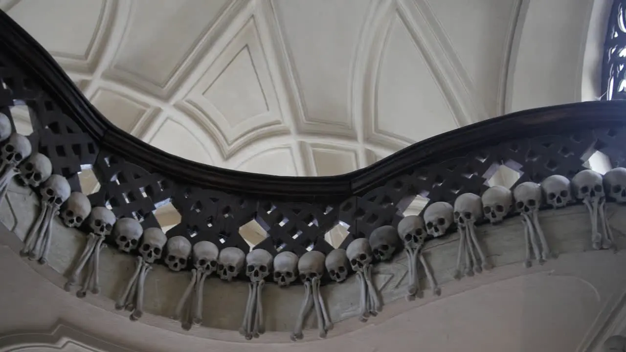 Panning shot across terrifying stair banister railing decorated with human remains skull bones in Sedlec Ossuary Roman Catholic Chapel Czech Republic