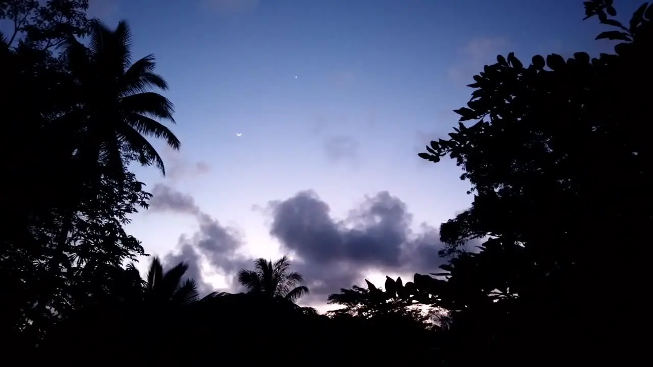 A crescent moon appearing on a time lapse as the sun has set and twilight colours show through