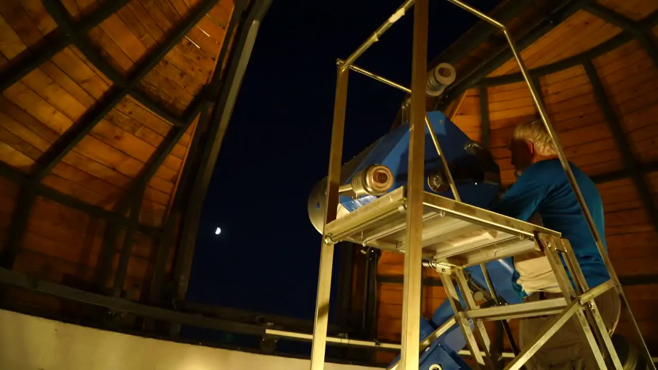 Man using large telescope in observatory to look at moon in night sky