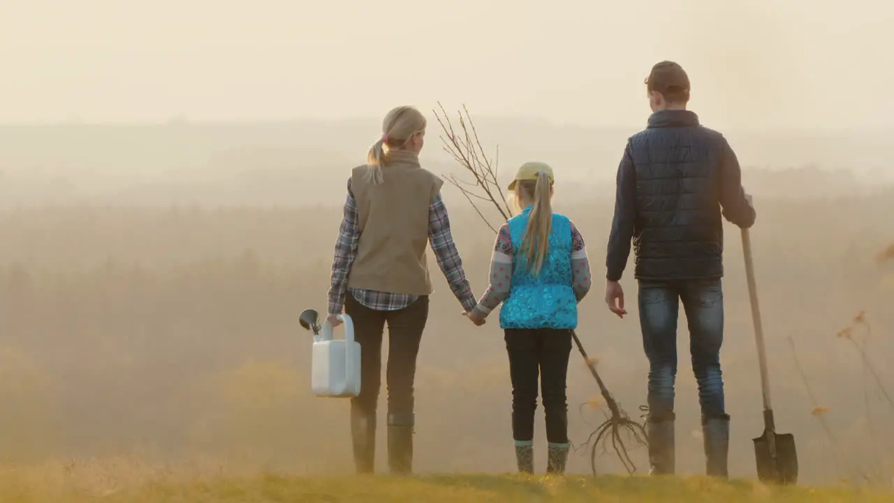 Family With A Tree Seedling A Sprinkler And A Shovel Standing In A Picturesque Place