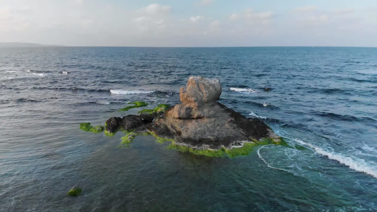 Aerial parallax shot around cliff in the sea at sunset