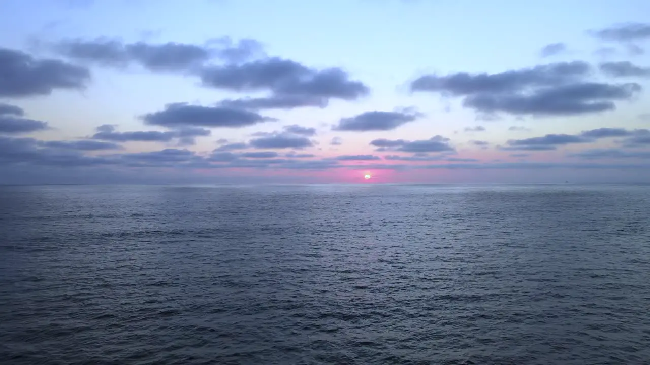 Low light scenic sunset above vast open ocean with several clouds in sky aerial