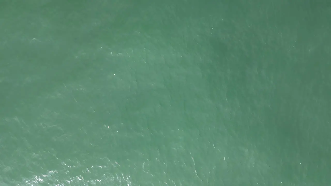 Aerial birdseye shot of a turquoise sea with calm waves reflecting the sun rays