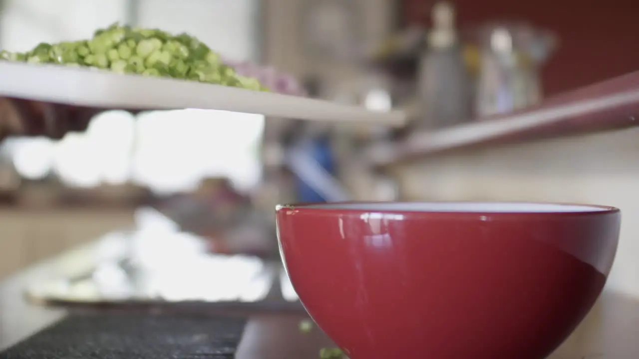 A chef scraping sliced spring onion into a red mixing bowl