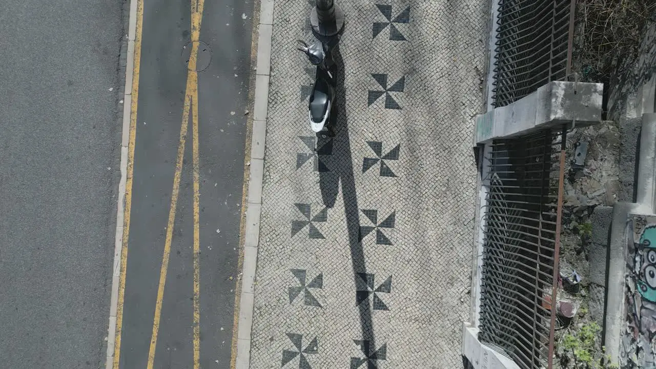 Art decorated sidewalk with two column triangular patterns and a motorbike parked beside the lamp post