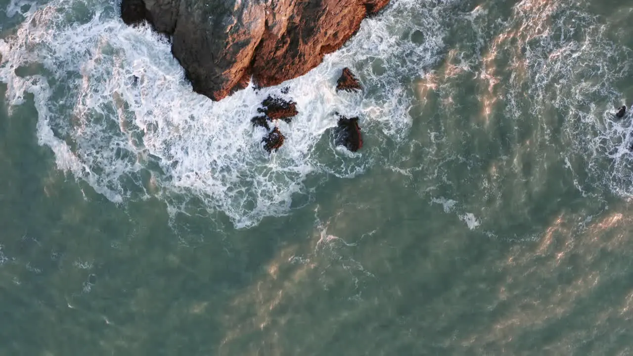 Birds Eye Aerial Shot of Waves Crashing against a Rocky Outcrop with Sea Lions at Sunset