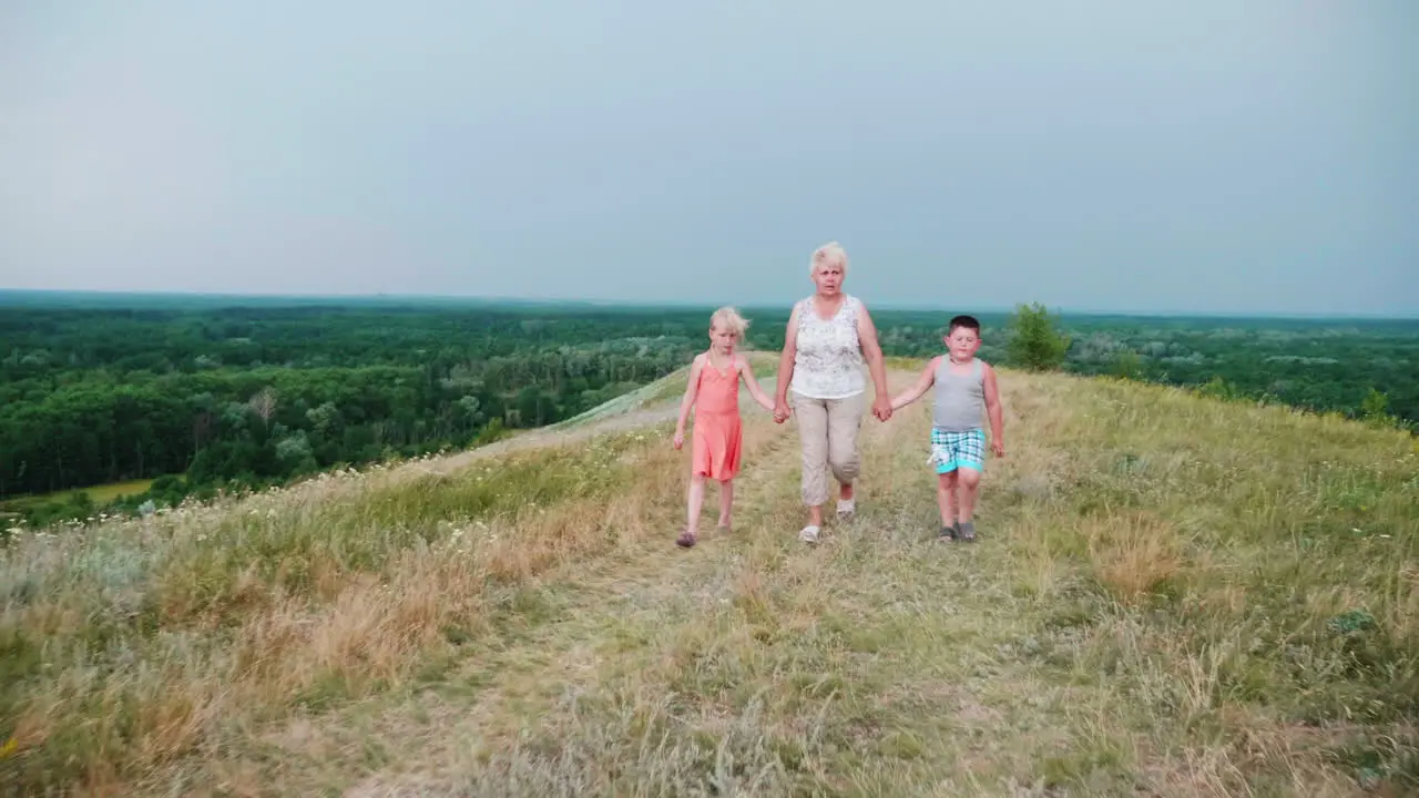 Grandmother For The Hands With Two Grandchildren A Girl And A Boy Walks Through The Lively Rural Countryside 1