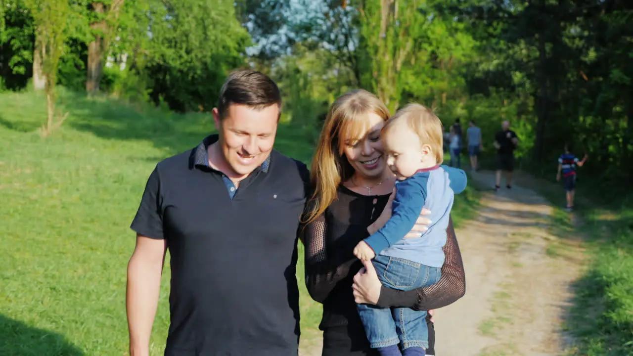 A Young Caucasian Family Is Walking With A Baby Son In The Park 1