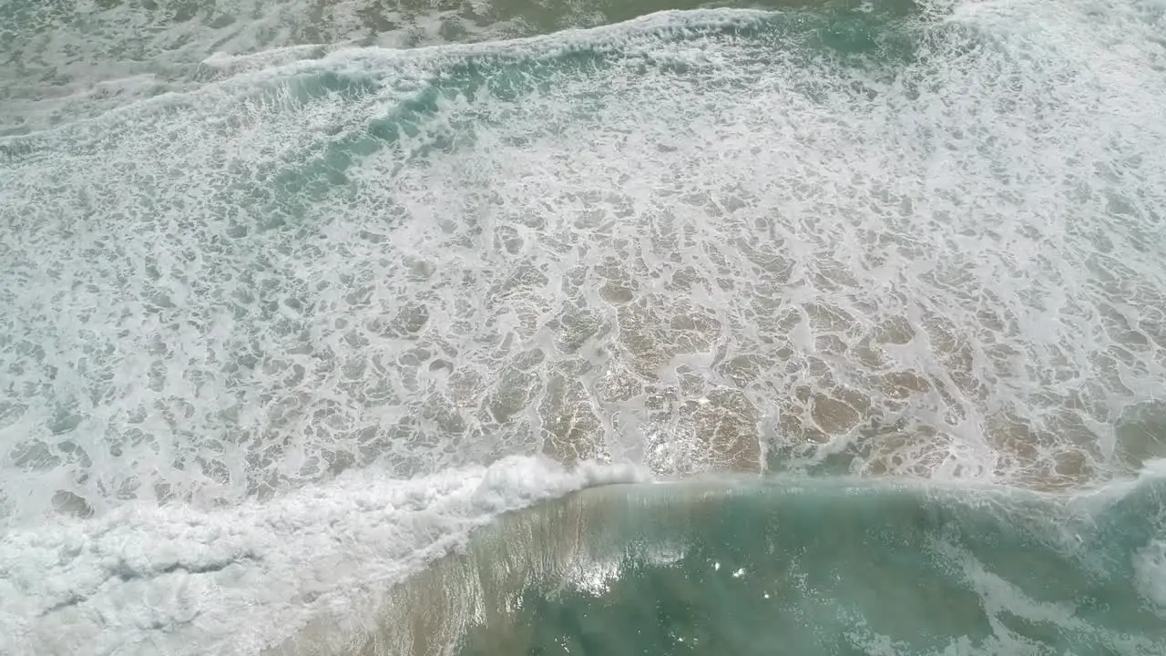 Following waves onto a beach with a drone high angle view