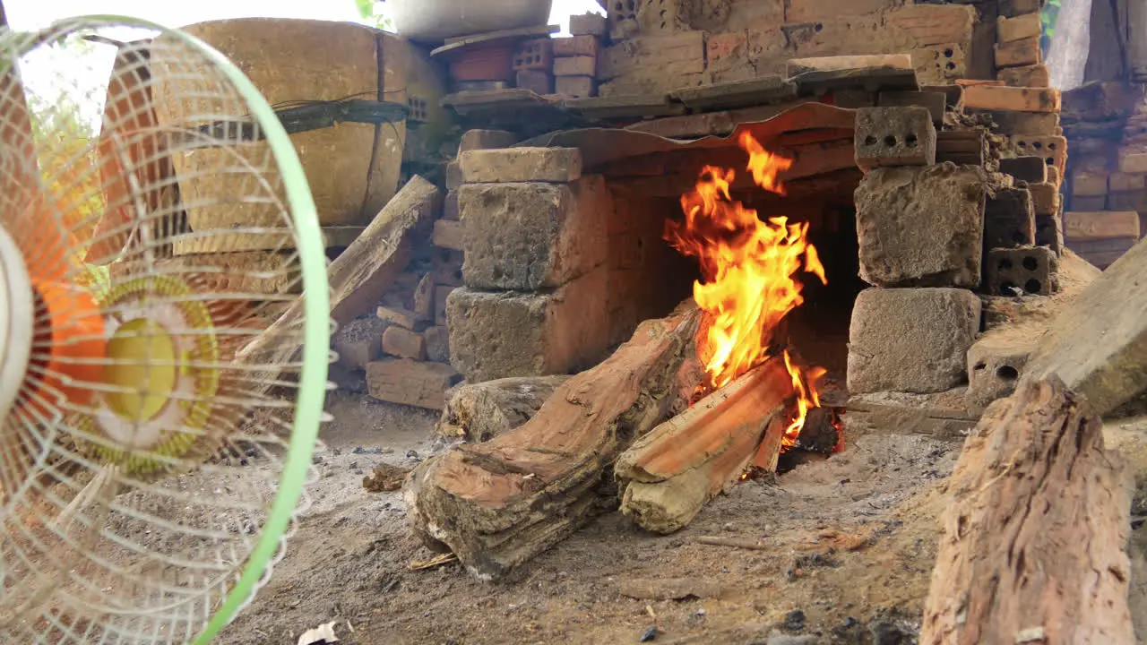 Low wide view of blazing wood fire in kiln fan blows fire and smoke Than Ha Vietnam Hoi An