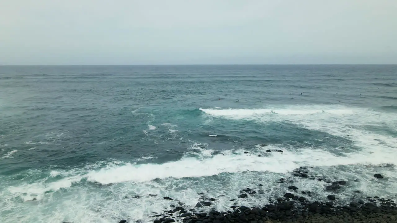 Ocean waves splash on rocky coast of Maui Island surfers waiting for wave