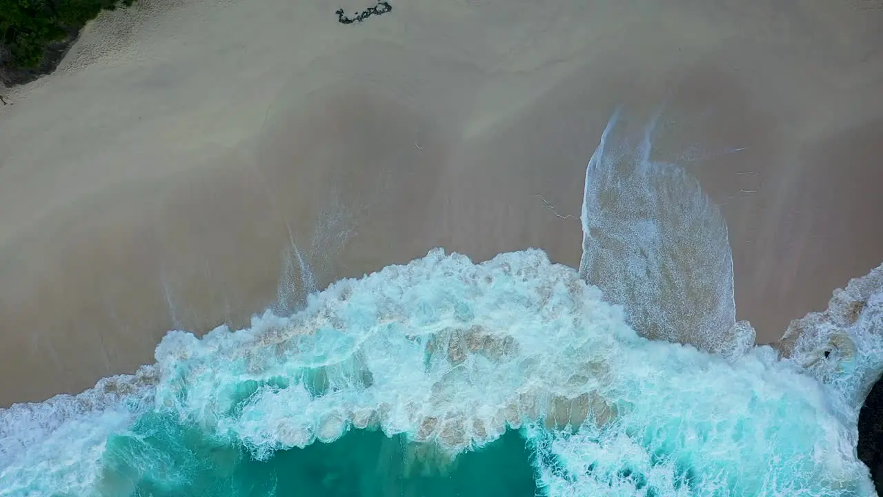 Aerial shot of turquoise ocean waves crashing white sand coastline of Kelingking Beach with azure lagoon and T-Rex Bay Nusa Penida one of the most popular tourist attraction near island Bali